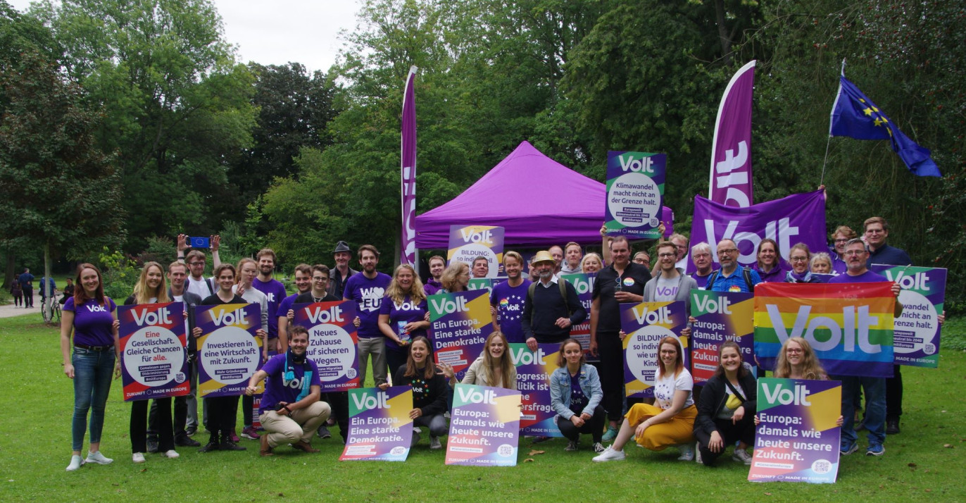 Gruppenbild vom Team Volt Düsseldorf im Volksgarten, mit lila Pavillon & Wahlplakaten vor der Landtagswahl 2022