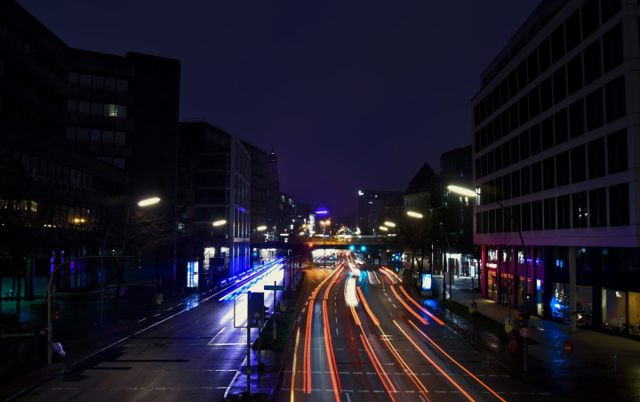 Willy Brandt Straße in Hamburg bei Nacht. In der Mitte ist eine beleuchtete Straße bei Nacht. Auf beiden Seiten links und rechts sind circa sechsstöckige Hochhäuser. Im Hintergrund ist eine Eisenbahnbrücke die von links nach rechts zieht. Die Schweinwerfer sind aufgrund einer Langzeitbelichtung über das Bild verschwommen