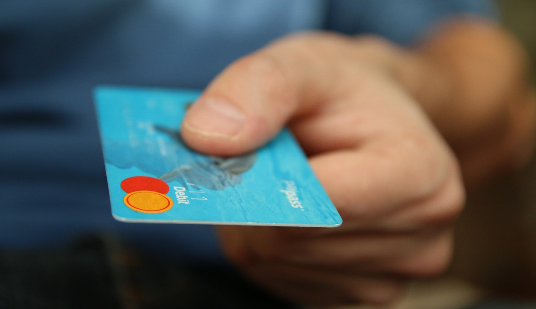Bild einer türkis-blauen Kreditkarte welche in der Hand eines Menschen gehalten wird.