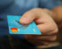 Bild einer türkis-blauen Kreditkarte welche in der Hand eines Menschen gehalten wird.